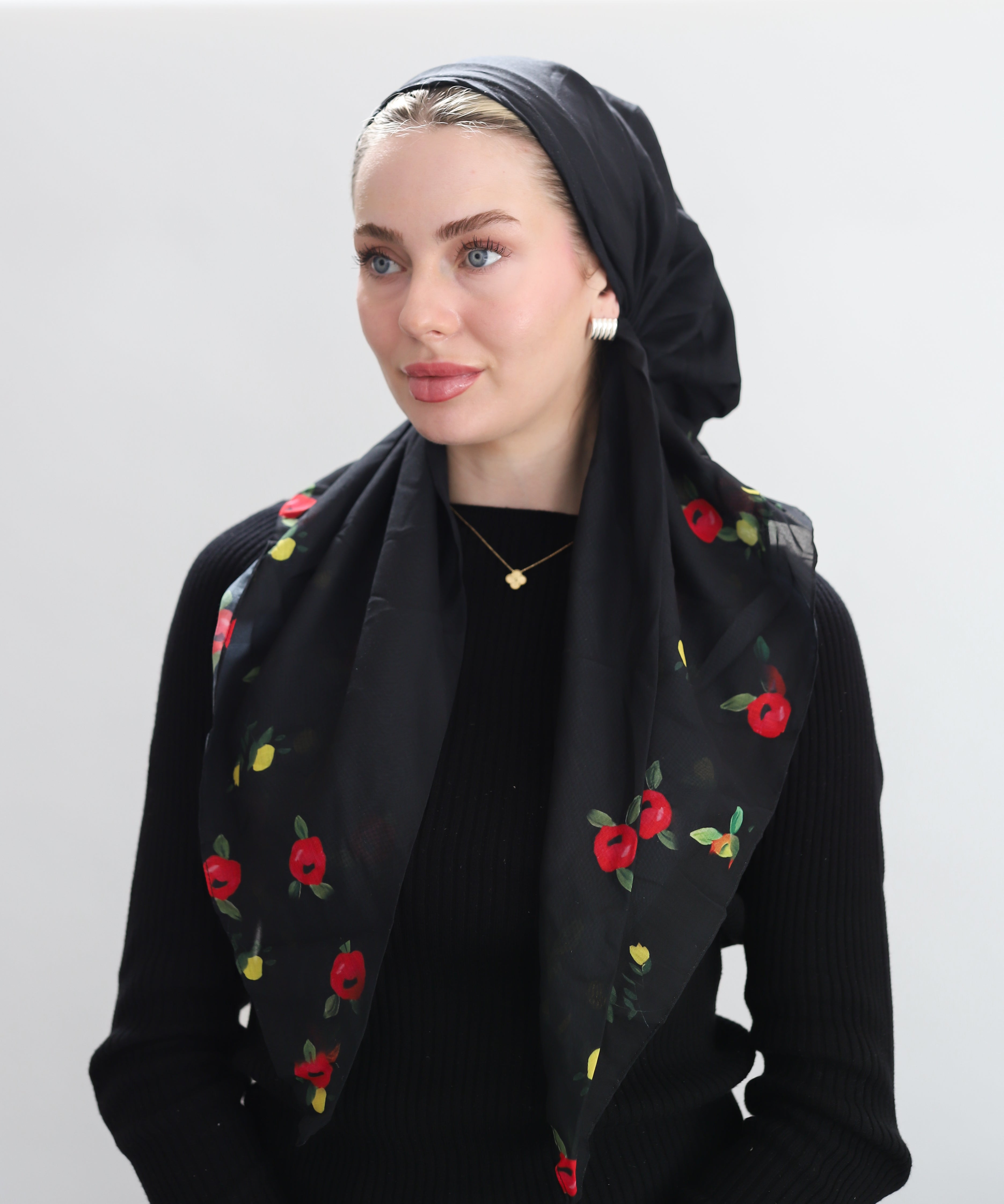 Woman wearing a black scarf with floral embroidery on a plain background